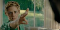Kristen Stewart mit blonden kurzen Haaren streckt zwei Finger von sich wie eine Waffe.