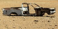 Ein verlassenes Autowrack steht ohne Räder in der Wüste