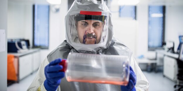 Mann mit Schutzanzug im Labor trägt vorsichtig Proben in Plastikhülle