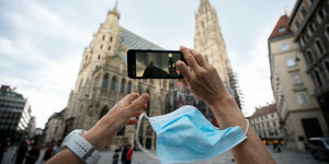 Mit Mundschutz an der Hand wird mit dem Smartphone ein Foto vom Stephansdom in Wien geschossen.