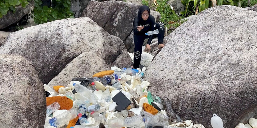 Steht zwischen zwei Felsen und wirft Plastikflaschen auf einen Haufen.