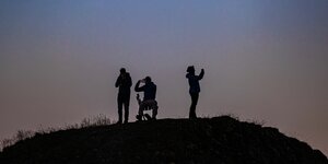 Menschen stehen auf einem Hügel und fotografieren den Sonnenaufgang