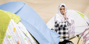 Eine afghanische Frau steht bedrückt zwischen Zelten