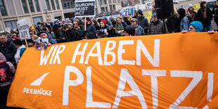 Das Bild zeigt ein orangefarbenes Spruchband bei einer Demo für die Aufnahme Geflüchteter im März in Berlin. Darauf steht: Wir haben Platz.