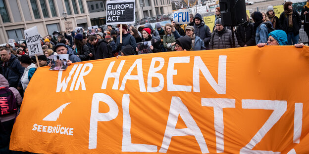 Das Bild zeigt ein orangefarbenes Spruchband bei einer Demo für die Aufnahme Geflüchteter im März in Berlin. Darauf steht: Wir haben Platz.