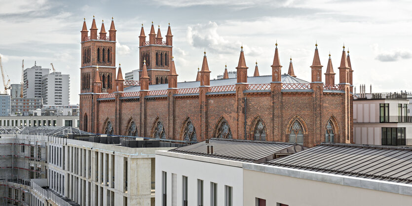 Die Friedrichswerdersche Kirche in Berlin-Mitte, davor eine Zeile mit den obersten Geschossen von Luxus-Neubauten