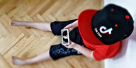 Ein Junge sitz auf dem Boden mit einer TikTok Cap und Handy in der Hand