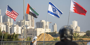 Eine Frau, die einen Mundschutz trägt, geht an der Friedensbrücke an den Flaggen der USA (l-r), der Vereinigten Arabischen Emirate, Israels und Bahrains vorbei