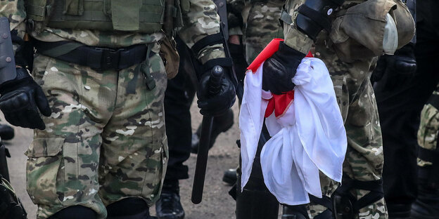 Sicherheitskräfte halten eine rot-weiße Flagge, die während eines Protests von Anhängern der Opposition in Minsk von Demonstranten beschlagnahmt wurde