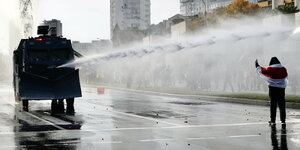 Ein Wasserwerfer zielt mit Wasser auf eine einzelne Demonstrantin
