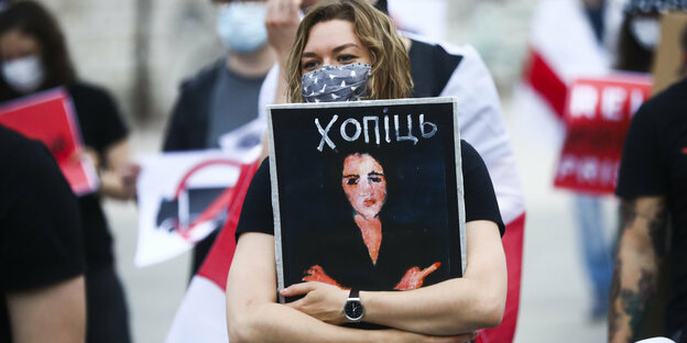 Eine Demonstrantin hält ein Schild in den Armen auf welchem das verfremdete Kunstwerk der Eva die einen Stinkefinker zeigt, zu sehen ist.