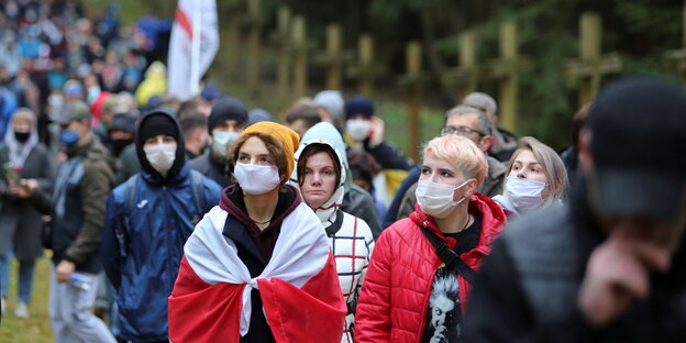 Oppositionelledemonstranten mit belarussischen Fahnen zieht während eines Marsches an den Holzkreuzen der Ermordeten in Kuropaty vorbei
