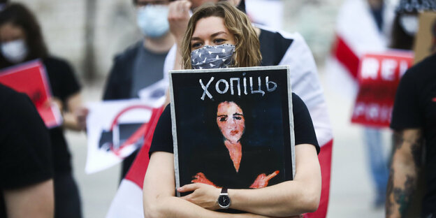 Eine Demonstrantin hält ein verfremdestes Bild der Eva, die einen Stinkefinger zeigt, in den Händen
