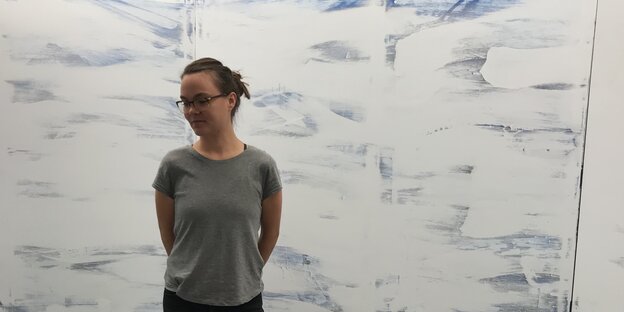 Die Künstlerin Anna Taina-Nielsen steht vor einer weißen Wand mit blauen Farbsptitzern