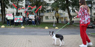 Eine Frau geht mit ihrem Hund spazieren. Im Hintegrund sieht man eine Gruppe Pro-Lukaschenko Demonstranten.