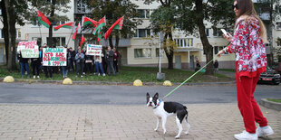 Eine Frau geht mit ihrem Hund spazieren. Im Hintegrund sieht man eine Gruppe Pro-Lukaschenko Demonstranten.