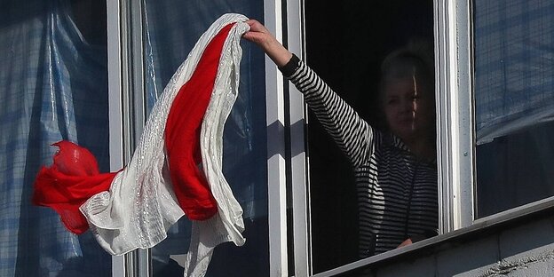 Eine Frau steht an einem Fenster und winkt mit einem weiß-roten Schal