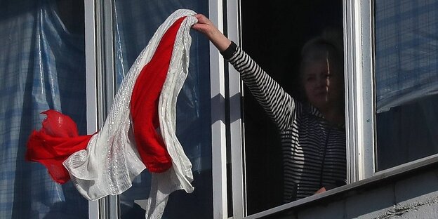 Eine Frau steht an einem Fenster und winkt mit einem weiß-roten SChal