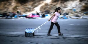 Mädchen zieht auf einer Straße einen Kasten mit Wasserflaschen hinter sich her