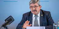 Innenminister Lorenz Caffier sitzt an einem Tisch vor einem Mikrofon. Der Hintergrund ist blau.