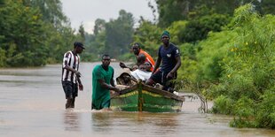 Menschen waten durch Wasser und schieben ein Boot, in dem ihre Haustiere sind