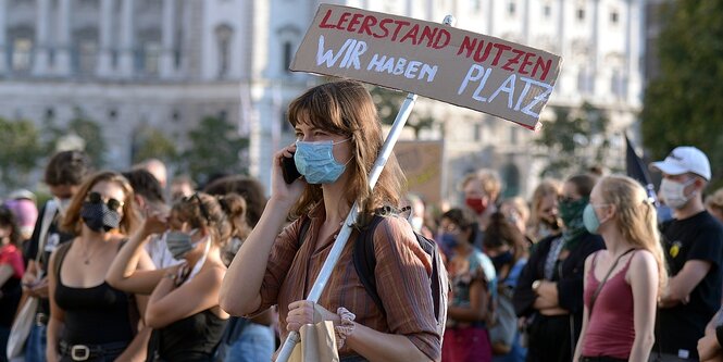 Menschen demonstrieren, eine Frau hält ein SChild mit der Aufschrift "Leerstand nutzen, wir haben platz"