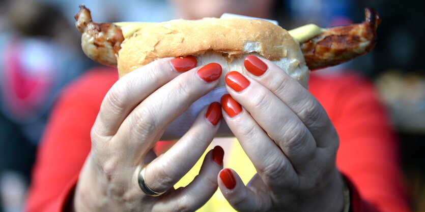 Eine Bratwurst im Brötchen in einer ausgestreckten Hand