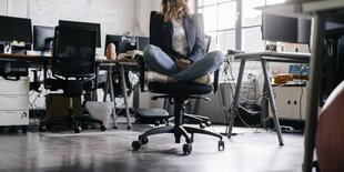 Eine Frau sitzt im Schneidersitz auf einem Bürostuhl