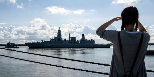 Eine Frau mit Zöpfen blickt auf ein Kriegsschiff