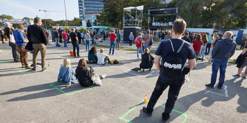 Konzertbesucher stehen mit Abstand zueinander vor einer Bühne.