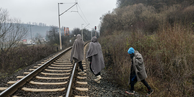 Drei Männeeingehüllt in Decken gehen auf Bahngleisen Richtung Kroatien