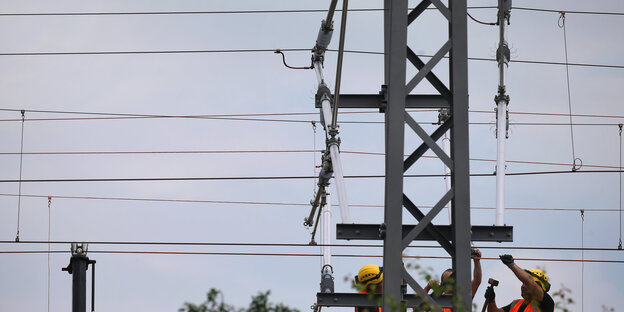 Auf dem Bild werkeln Arbeiter mit Bauhelmen an einer Strom-Oberleitung herum.