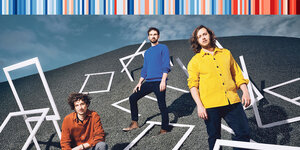 Die Mitglieder der Hamburger Band Helden in blauem, gelben und roten Hemd zwischen leeren weißen Bilderrahmen