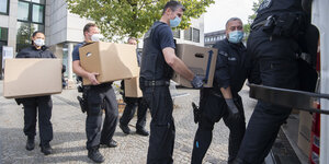 PolizistInnen bringen Kartons mit bei der Razzia sichergestellten Unterlagen zu ihrem Einsatzfahrzeug