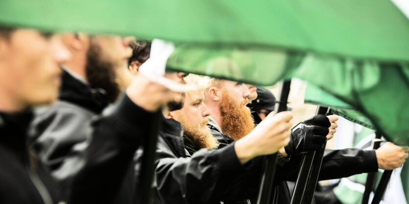 Neonazis stehen dicht nebeneinander und halten grün-weisse Fahnen