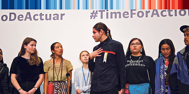 sechs Menschen of Colour und Luisa Neubauer stehen vor einer Wand mit dem 'TimeforAction". Eine der