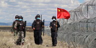 Chinesische soldaten auf Pa­t­rouil­le mit Fahne neben Stacheldraht