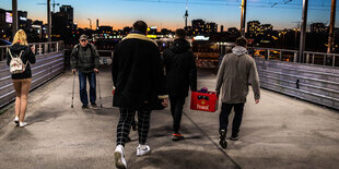 Junge Menschen mit Bierkasten vor Stadtkulisse.