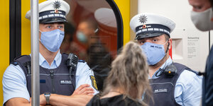 Zwei Polizisten mit Atemschutzmaske stehen in einer U-Bahn