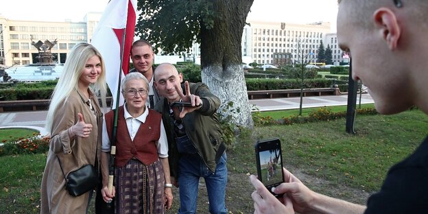 Ein mann macht ein handyfoto von einer Gruppe vión vier Menschen, in der Mitte steht eine alte Frau