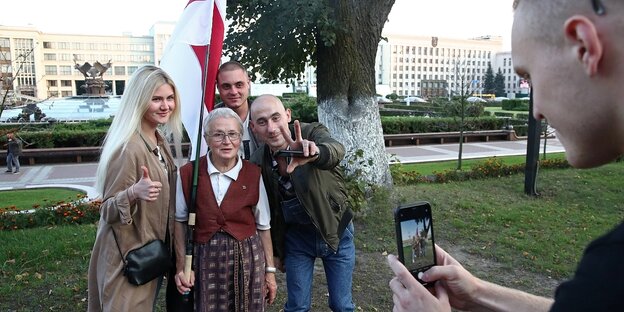 Ein Mann macht ein Handyfoto von einer Gruppe von vier Menschen, in der Mitte ist Nina Baginskaja