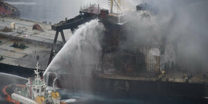 Ein Löschschiff sprüht Wasser auf den Öltanker, der vor der Küste von Sri Langa brennt. Dichter Rauch steigt auf.