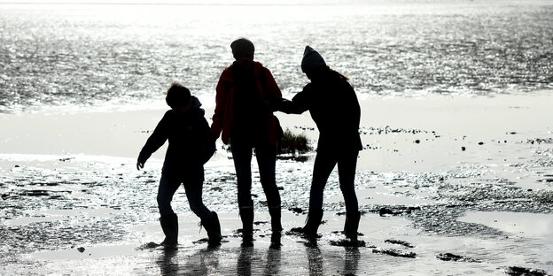 Zwei Erwachsene und ein Kind spazieren am Meer