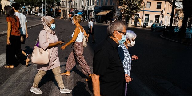 Menschen tragen Mundschutzmasken und überqueren eine Straße