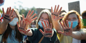 Frauen halten Hände hoch, die sie mit Worten beschriftet haben