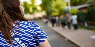 Eine junge Frau, Rückenansicht, trägt ein T-Shirt im Aldi-Logo-Muster, weiter hinten sieht man die Warteschlange