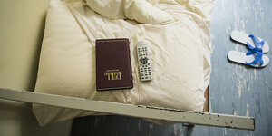 Vogelperspektive auf ein Bett, auf dem eine Bibel und eine Fernbedienung liegen