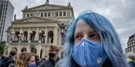 Eine junge Frau mit blauen Haaren und einer blauen Mundschutzmaske demonstriert