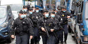 Uniformierte Männer mit Mundschutzmasken und Gewehren gehen eine Straße entlang