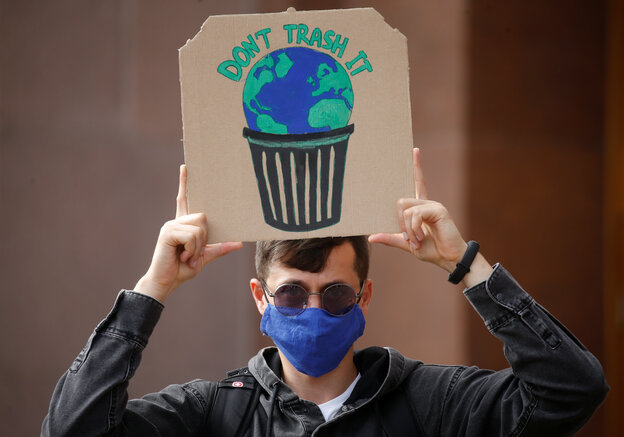 Junger Mann mit Maske hält ein Pappschild auf dem eine Erde gemalt ist, die in einem Papierkorb liegt, darüber der Schriftzug "Don't trash it"